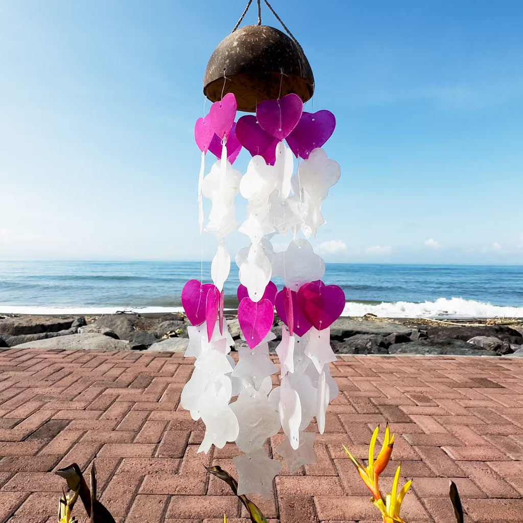 Handcrafted coconut shell wind chime with pink and white capiz shell hearts hanging by the sea