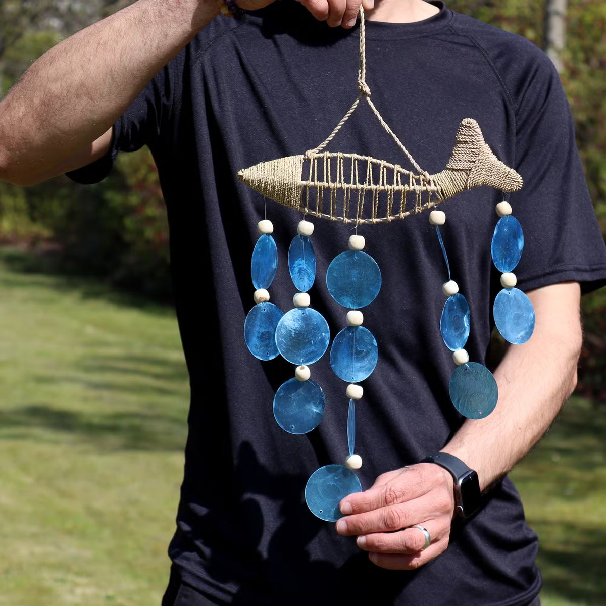 Man holding handcrafted string fish blue copis drop wall decoration to show size, coastal home decor