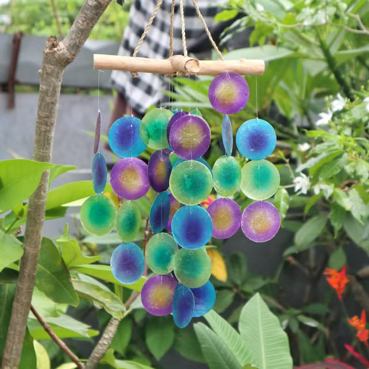 Green purple and blue capiz shell garden wind chime hanging from bamboo in tropical outdoor garden