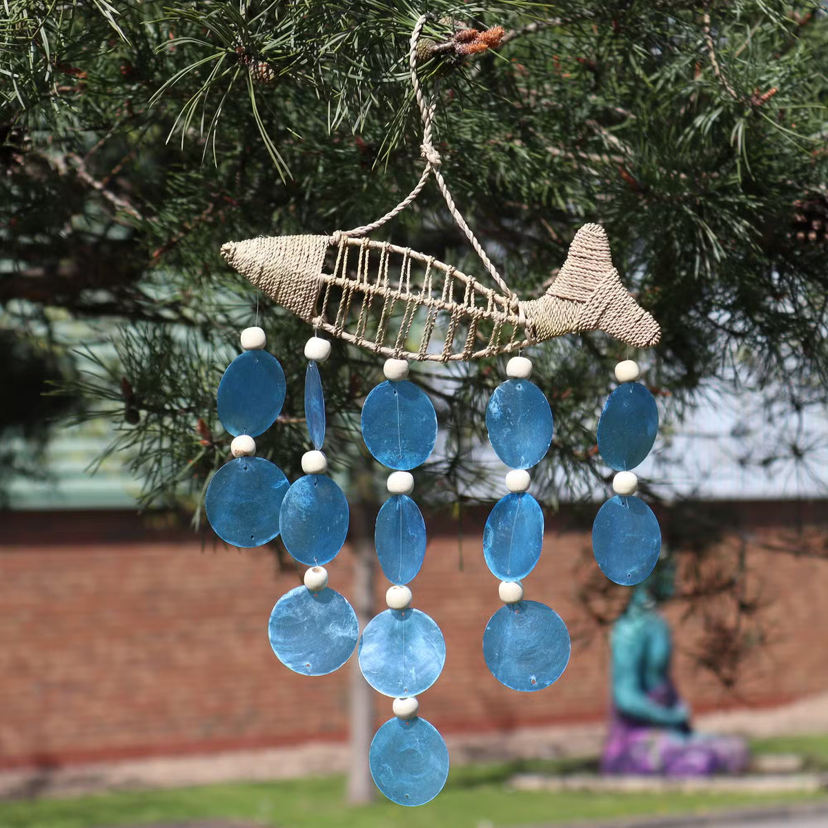 Handcrafted woven string fish wall hanging with blue copis shell drops and wooden beads, outdoor garden display