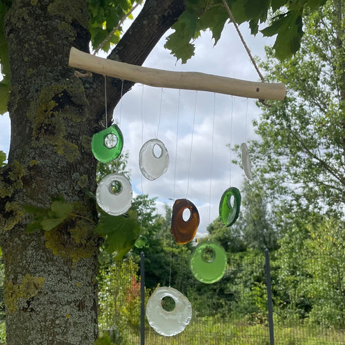 Bottle bottoms glass wind chime hanging from tree in garden — green, clear and amber recycled glass bottle bottoms on driftwood bar