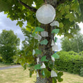 Copis and glass drop wind chime — full view hanging from tree with green and white sea glass pieces against garden backdrop
